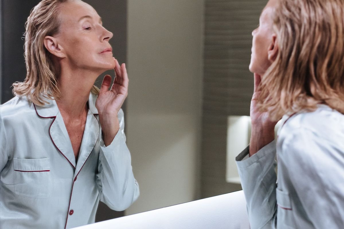 A woman applying skincare at a bathroom mirror