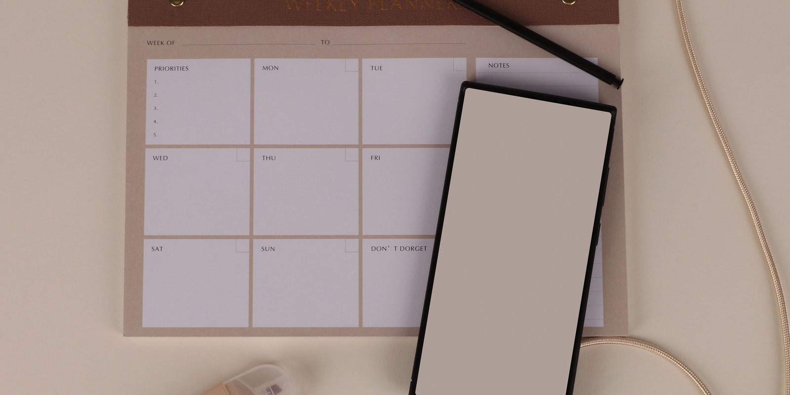 A weekly planner, pencil and tablet laid out on a neutral surface