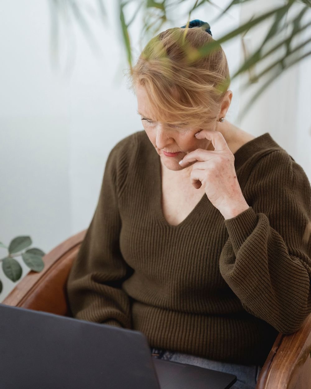 A woman sitting in an armchair at home, resting her head on her hand while working